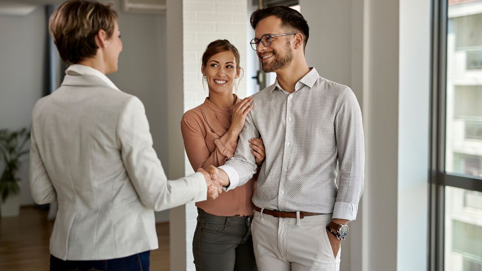 smiling man and woman shaking hands with a woman in a pantsuit